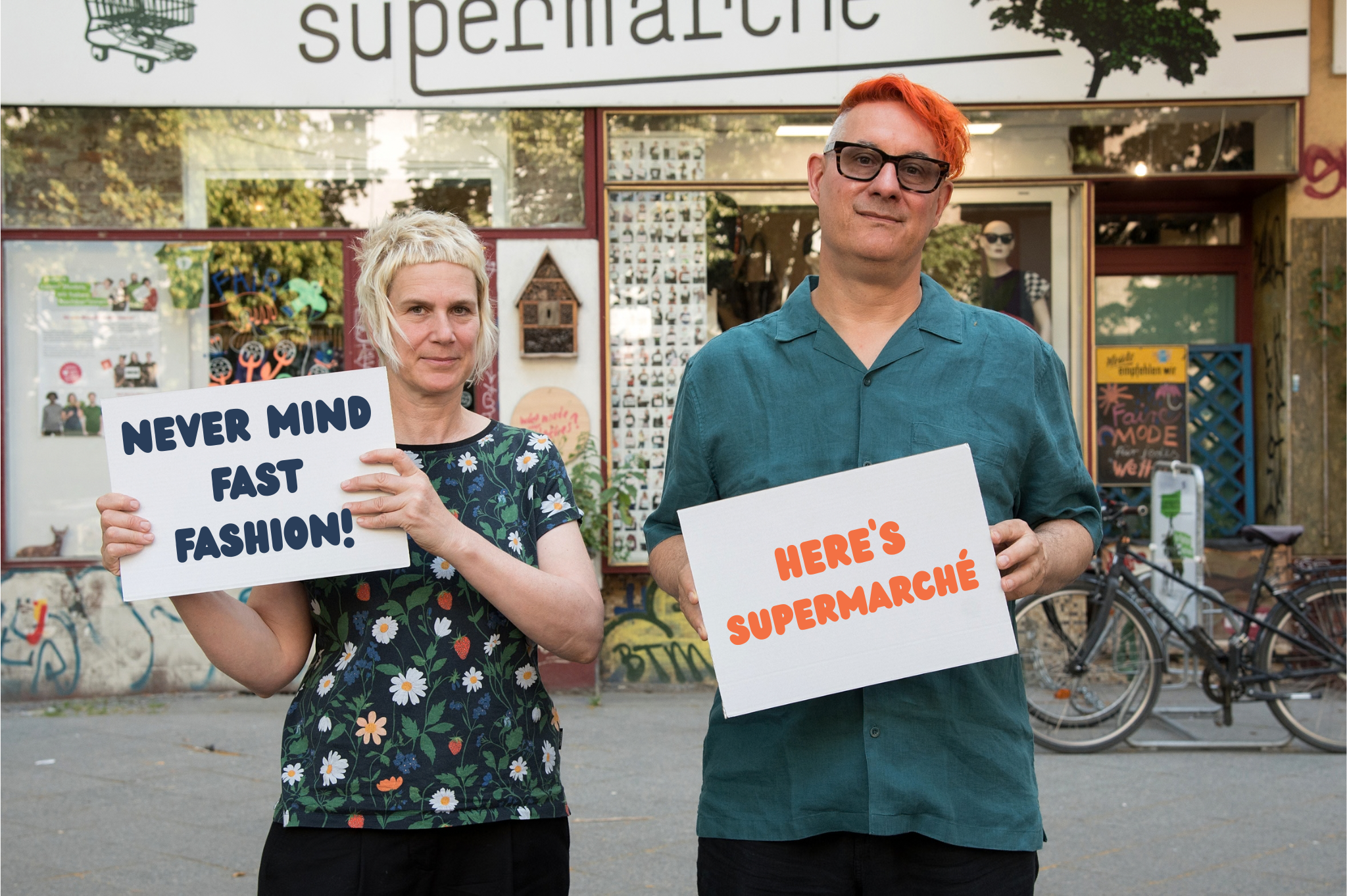 2 Personen stehen vor dem supermarché und halten Schilder mit der Aufschrift "Never mind Fast Fashion!" und "Here's supermarché"